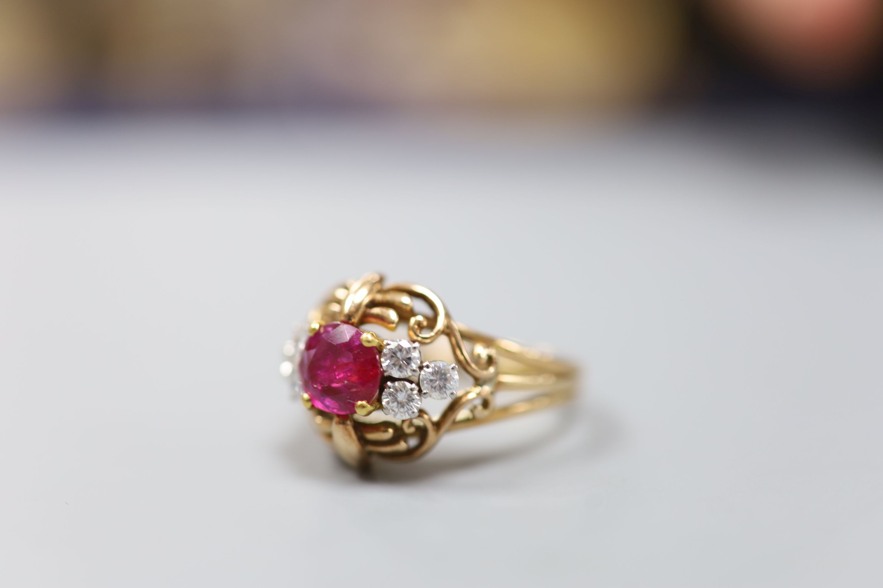 A stylish yellow metal, ruby and diamond set cluster ring, with single round cut ruby(crack), flanked by six round cut diamonds, in an openwork scroll setting, size Q/R, gross weight 7.5 grams, in a Cartier box.